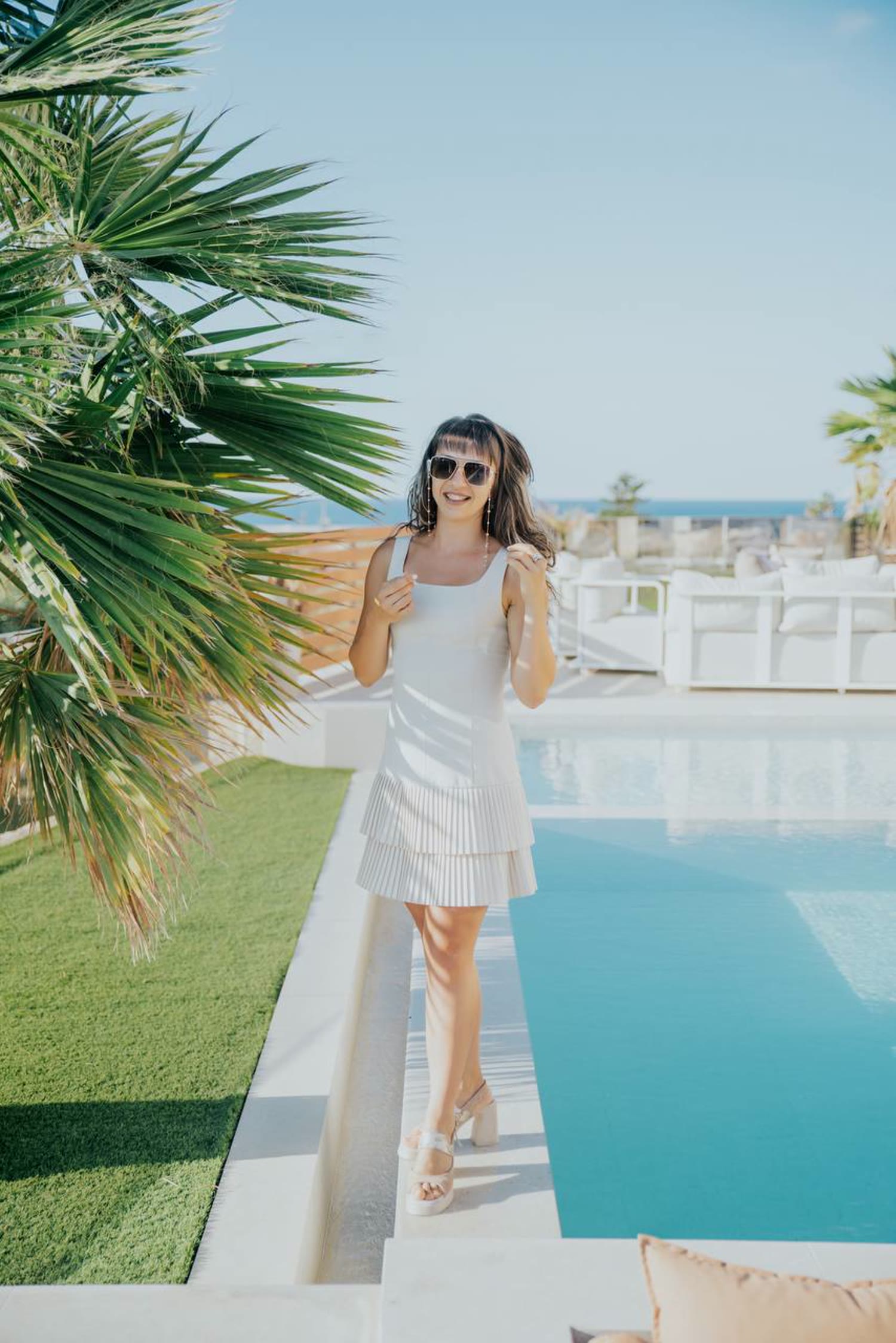 Marchela in a white dress beside a pool overlooking the ocean and sky